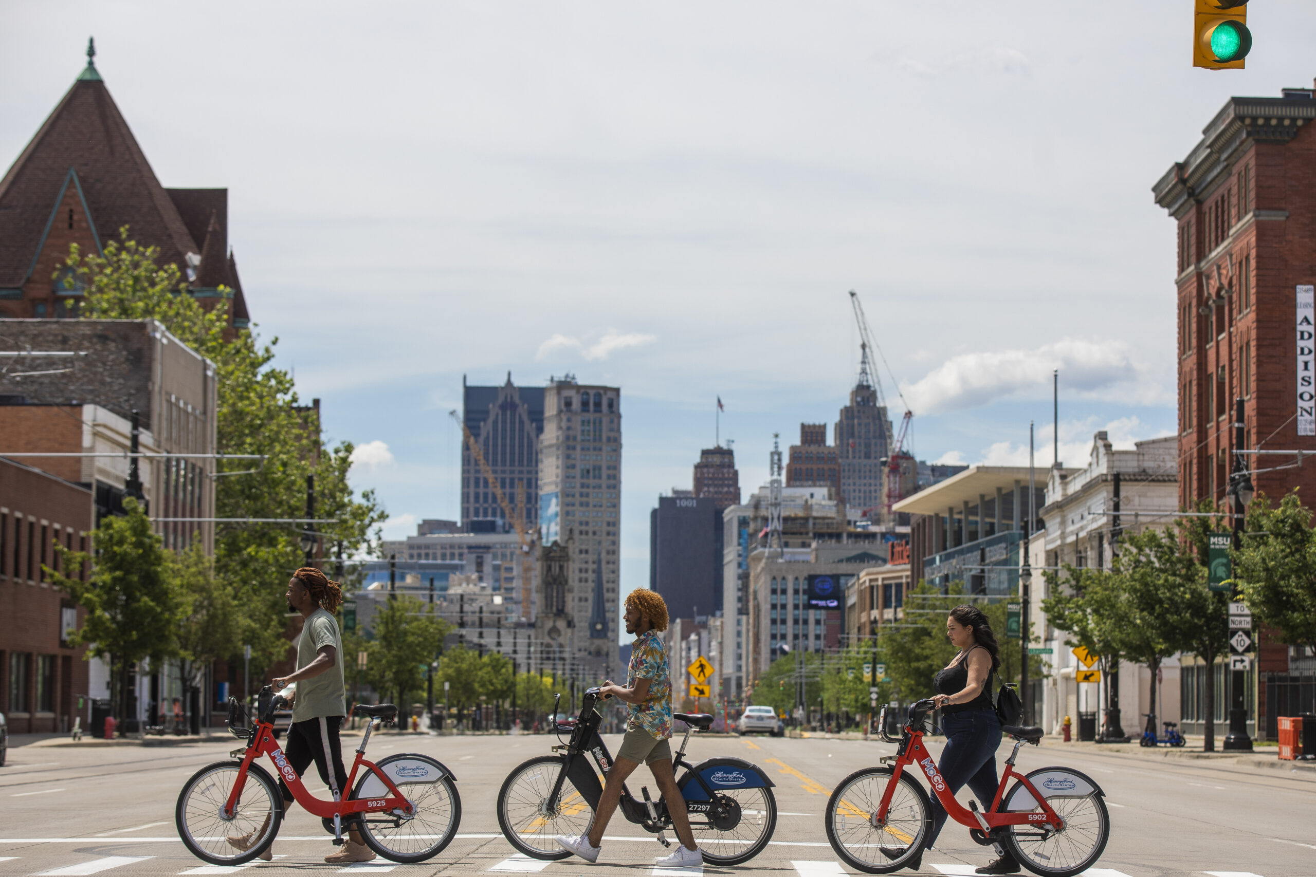 Group of three friends crossing crosswalk with their bikes in tow, located at Detroit's Brush Patk