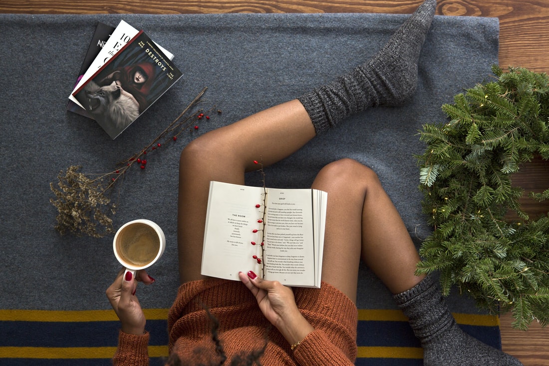 Woman sits reading books wearing cozy socks and with a cup of coffee in hand