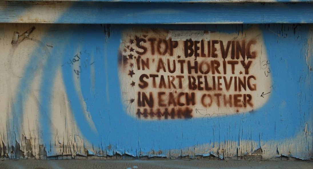 graffiti on a wall saying: "Stop believing in authority, start believing in each other."