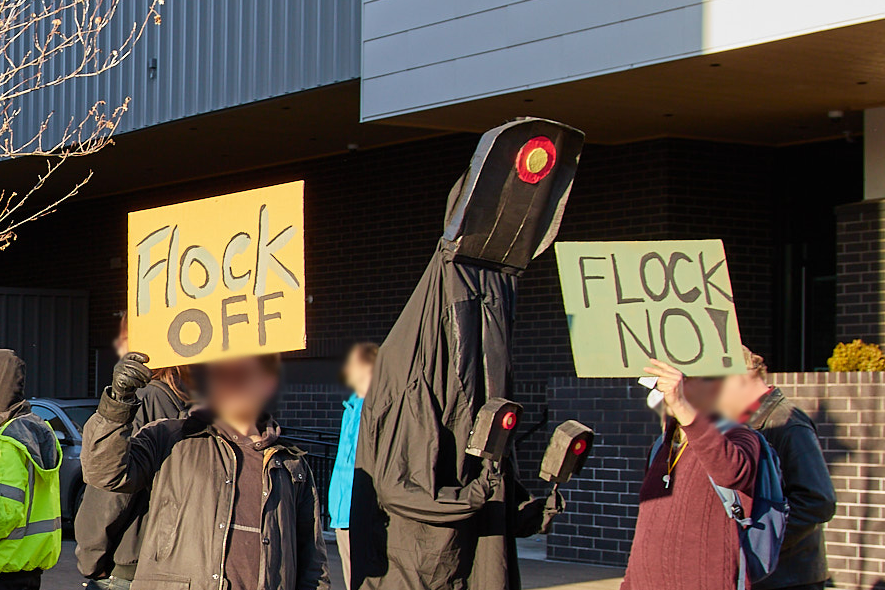 An anti Flock protest in Ithaca with a protestor dressed up as a flock camera with signs that read, "Flock Off' and "Flock no!"